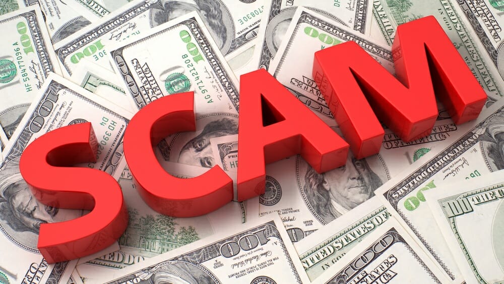 Hundred dollar bills with the word "scam" in big red letters sitting on top.